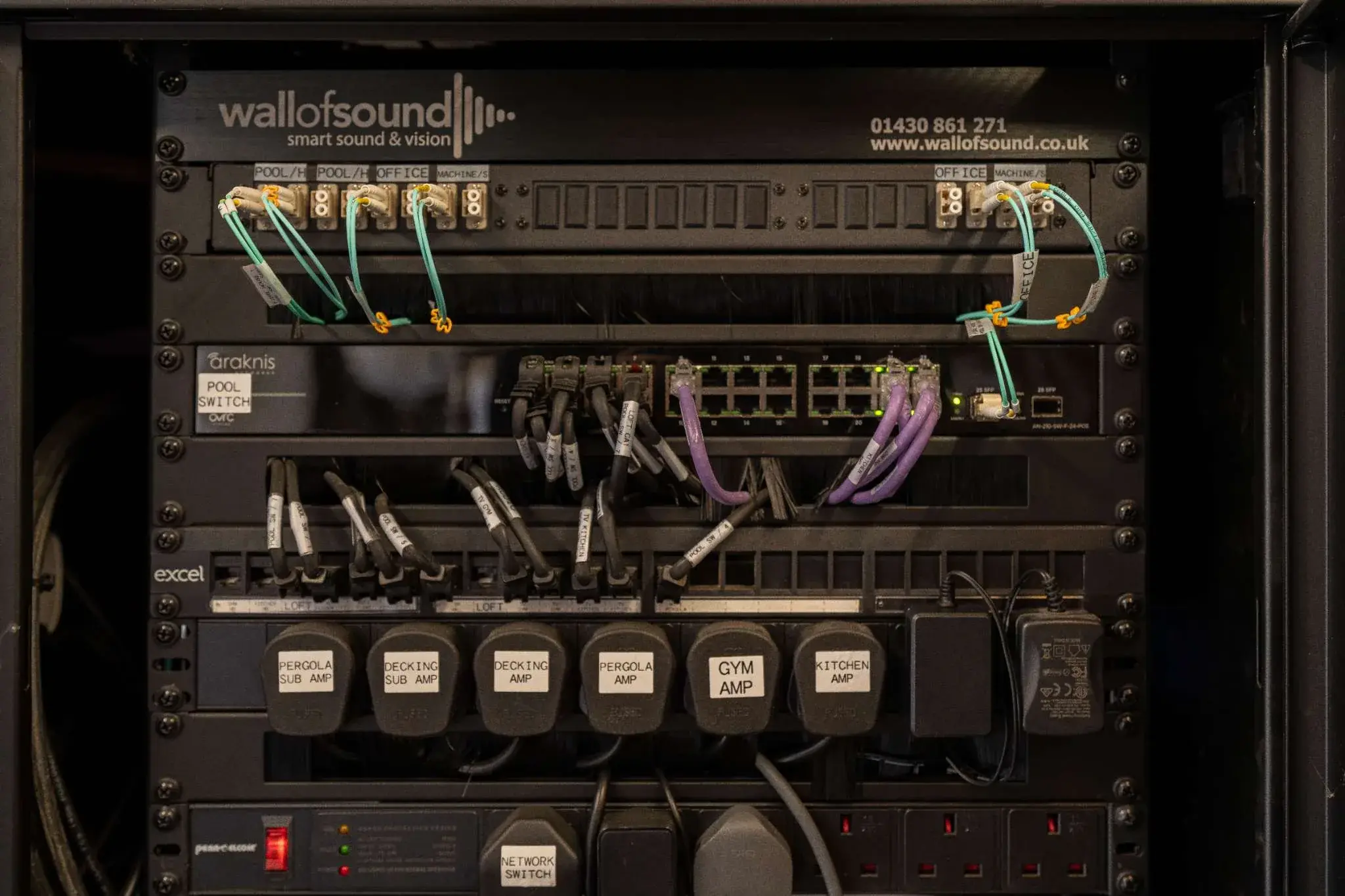 A Wall of Sound equipment rack: network switch and zone amplifiers labelled by area of the house